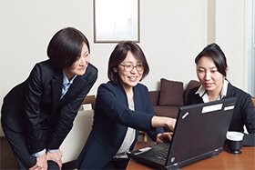 オフィスで3人の女性がノートパソコンを囲んで作業している様子
